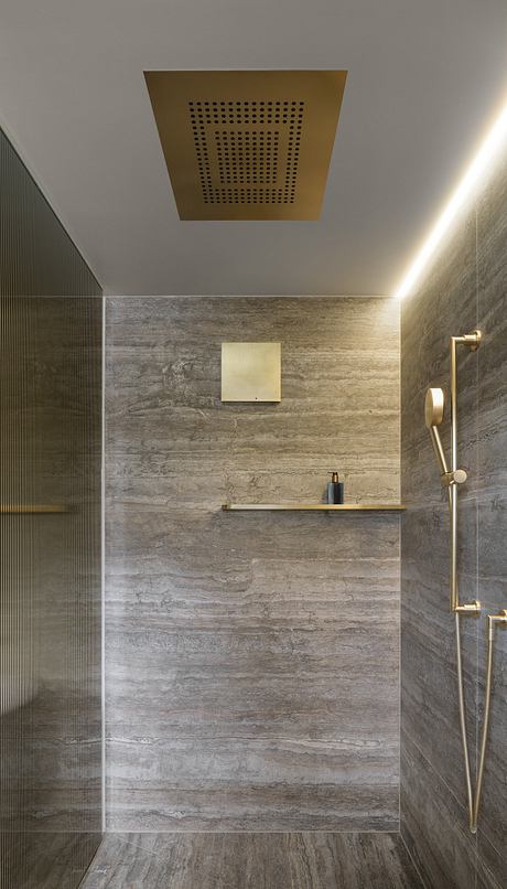 Modern shower room with gray textured walls, gold fixtures, and a minimalist square shower head.