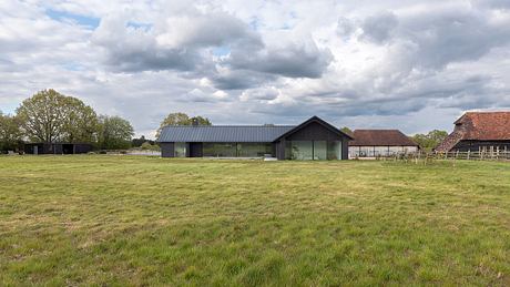 Modern farmhouse-style building with large windows overlooking a grassy field and wooded area.