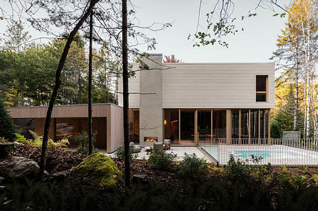 Modern residential structure with wood siding, expansive glass walls, and an outdoor pool nestled in a forested setting.