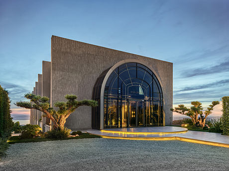 Striking modern architecture with a dramatic glass-arched entryway and lush landscaping.