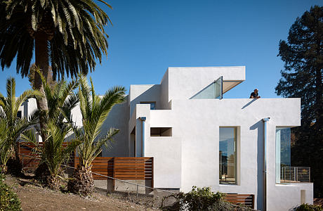 Modern, angular white home with wooden accents and palm trees in the foreground.