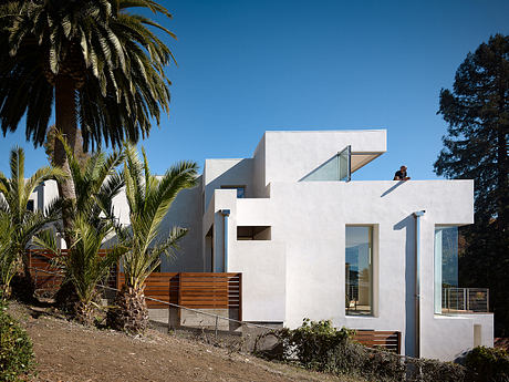 Modern, angular white home with wooden accents and palm trees in the foreground.