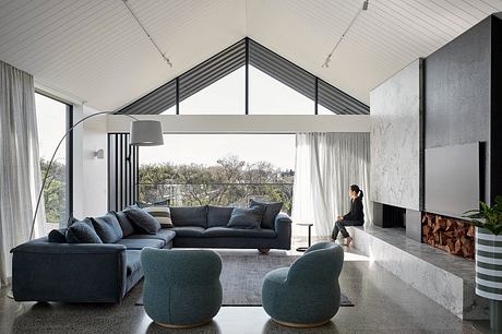 A modern, high-ceilinged living room with a large L-shaped sofa, armchairs, and a fireplace.