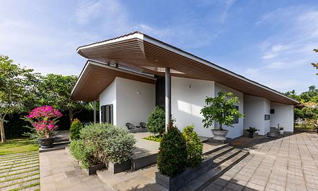 A modern single-story home with a slanted roof, patio, and lush landscaping.