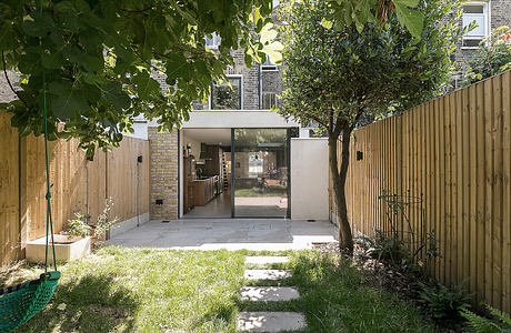 A modern glass-and-brick entryway opens to a lush backyard with paving stones and greenery.