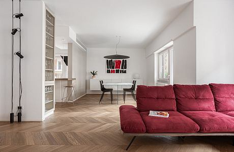 Minimalist interior with red sofa, geometric wall art, and built-in shelving. Hardwood floors and pendant lighting.