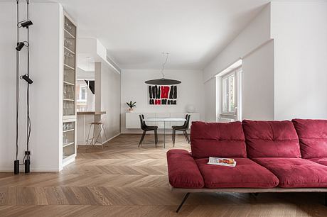 Minimalist interior with red sofa, geometric wall art, and built-in shelving. Hardwood floors and pendant lighting.