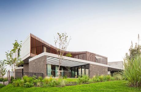 A modern architectural structure featuring a combination of concrete, wood, and glass elements, surrounded by a lush green landscape.