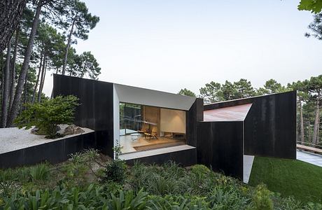 A sleek, modern cabin with a recessed balcony surrounded by lush greenery.