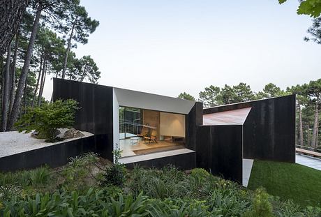 A sleek, modern cabin with a recessed balcony surrounded by lush greenery.