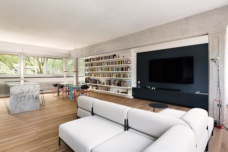 Sleek, modern living space with bookshelves, TV, and large windows overlooking nature.