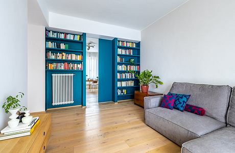 Vibrant blue built-in bookshelves flank a doorway, contrasting with wooden floors and gray sofa.