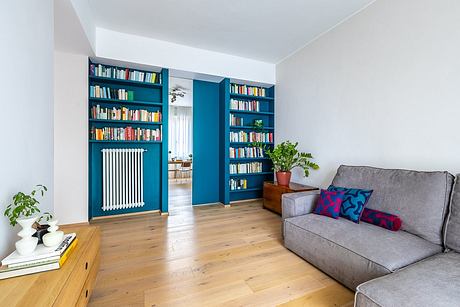 Vibrant blue built-in bookshelves flank a doorway, contrasting with wooden floors and gray sofa.