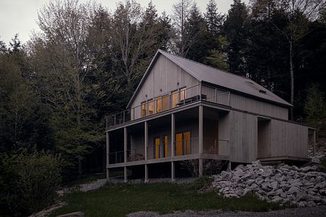 A modern cabin-style home with a wraparound porch and warm interior lighting.