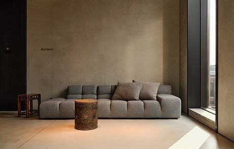 Minimalist living room with large gray sofa, ornate side table, and expansive windows.