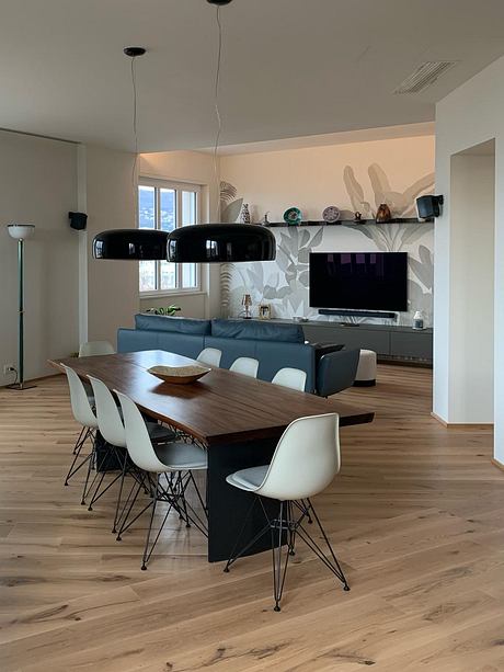 A spacious, modern living room with a wooden dining table, white chairs, and a stylish TV wall.