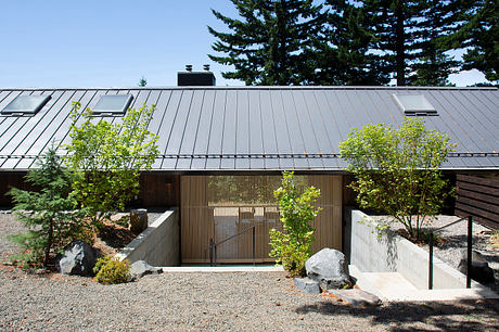 A contemporary building with a metal roof, wooden siding, and a gravel courtyard surrounded by trees.