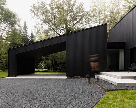 A modern, black wooden structure with a flat roof and glass walls, set in a lush, forested environment.