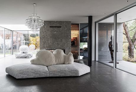 Large, modern living room with plush gray sofa, crystal chandelier, and glass walls overlooking nature.