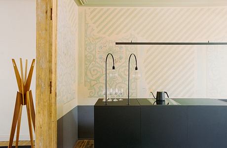 A modern bar area with a black counter, hanging light fixtures, and an ornate patterned wall.