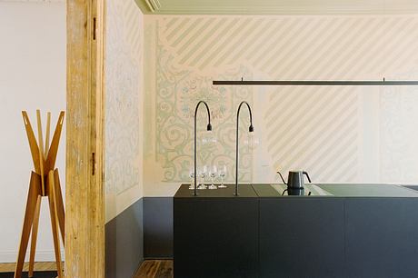 A modern bar area with a black counter, hanging light fixtures, and an ornate patterned wall.