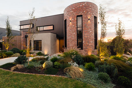 Modern brick and glass home with a well-designed landscaped yard at sunset.