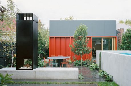 Modern outdoor patio with sleek gray siding, vibrant orange accents, and lush greenery.