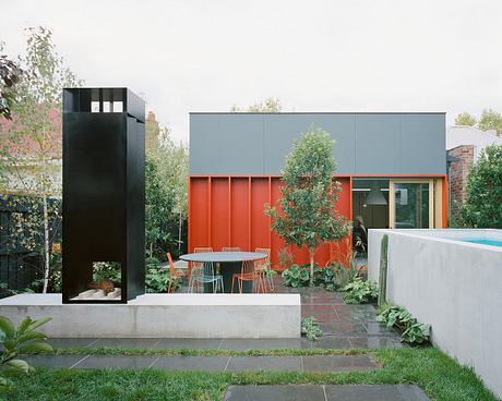 Modern outdoor patio with sleek gray siding, vibrant orange accents, and lush greenery.