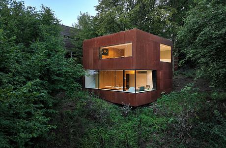 A modern, rectangular home nestled among lush foliage, with large windows offering a panoramic view.