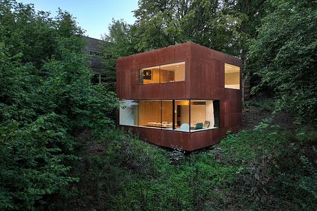 A modern, rectangular home nestled among lush foliage, with large windows offering a panoramic view.