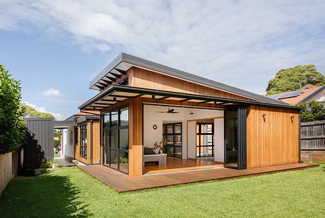 A modern, open-concept home with a wooden exterior and large windows overlooking a grassy yard.