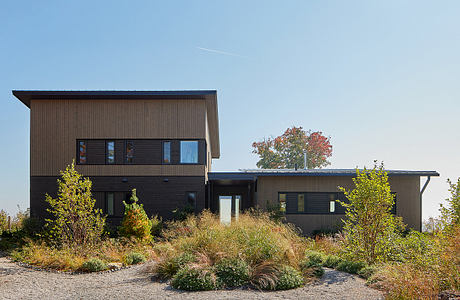 A modern, two-story house with dark siding, large windows, and a landscaped yard.