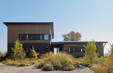 A modern, two-story house with dark siding, large windows, and a landscaped yard.