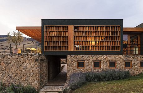 A modern architectural marvel with a striking wooden facade, stone walls, and a lush landscape.