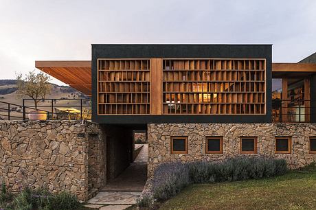 A modern architectural marvel with a striking wooden facade, stone walls, and a lush landscape.