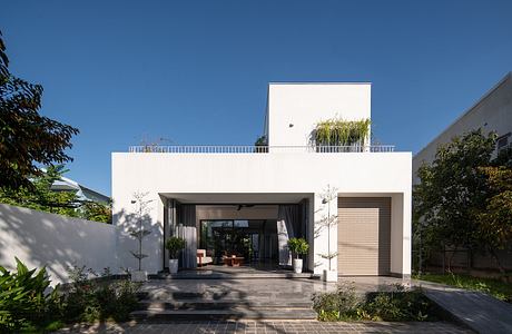 Modern white building with a recessed entryway, balcony, and lush greenery surrounding the exterior.