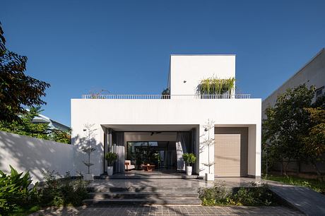 Modern white building with a recessed entryway, balcony, and lush greenery surrounding the exterior.