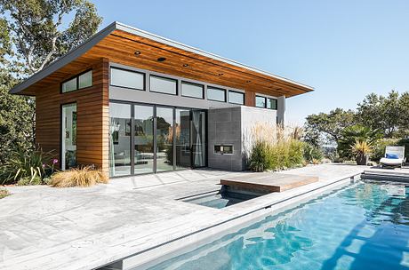 Modern, open-concept house with expansive windows, wooden siding, and a swimming pool.