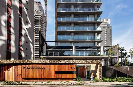 Modernist high-rise with glass balconies, stone base, and recessed entrance canopy.