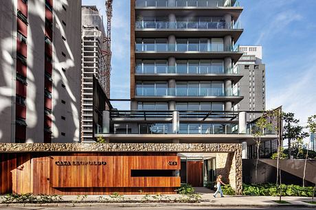 Modernist high-rise with glass balconies, stone base, and recessed entrance canopy.