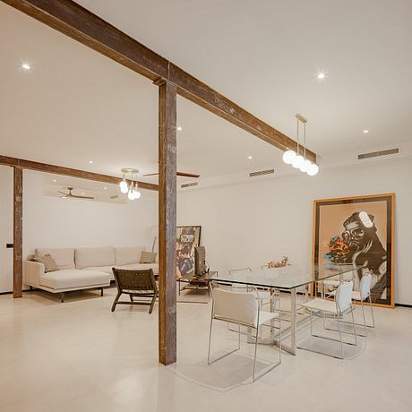 Expansive, modern interior featuring exposed wooden beams, glass table, and artwork.