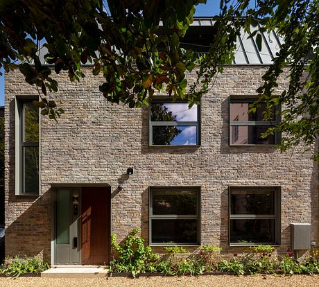 Brick façade with large windows, recessed entryway, and lush foliage surrounding the building.