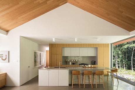 Spacious modern kitchen with clean lines, wooden accents, and large windows overlooking nature.