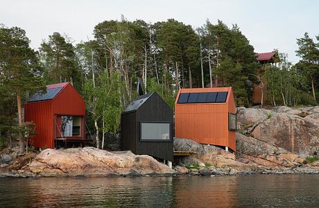 A cluster of modern, colorful cabins nestled in a forested landscape by the water.