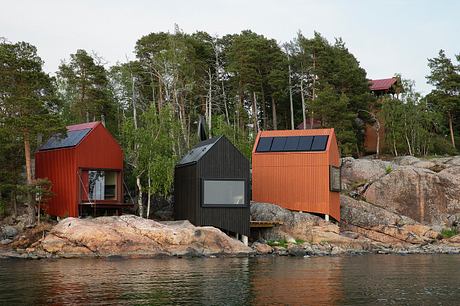 A cluster of modern, colorful cabins nestled in a forested landscape by the water.