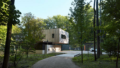 Sleek, modern architecture nestled in a lush, wooded environment with a gravel pathway leading to the entrance.