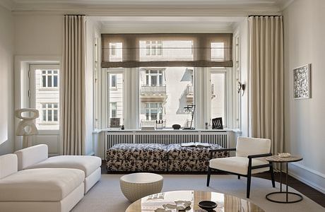 A cozy living room with ornate moldings, large windows, and a modern furniture arrangement.