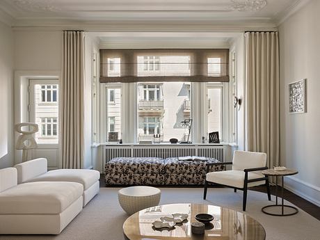 A cozy living room with ornate moldings, large windows, and a modern furniture arrangement.