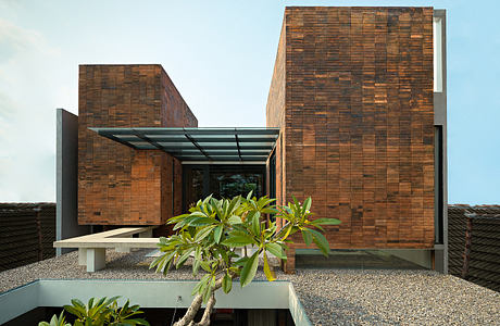 Modern architecture with textured brick facade, glass canopy, and lush tropical plants.