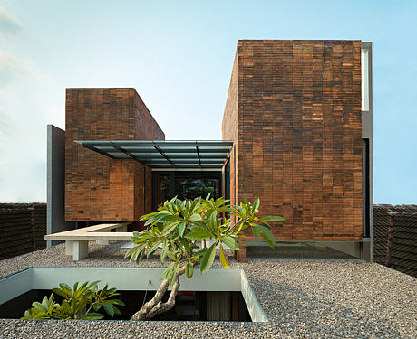 Modern architecture with textured brick facade, glass canopy, and lush tropical plants.